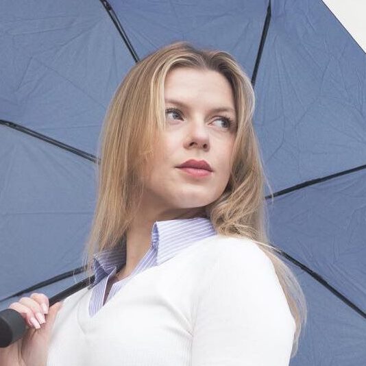 Profilbild einer blonden Frau mit blauem Regenschirm